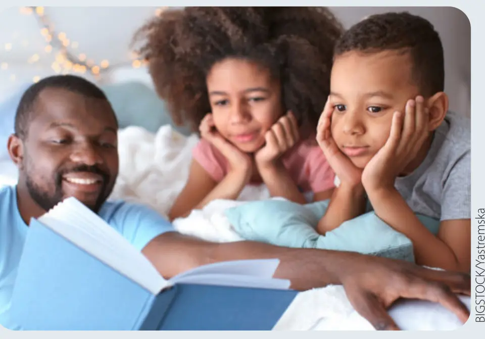 A father reading to two children in bed. (BIGSTOCK/Yastremska)