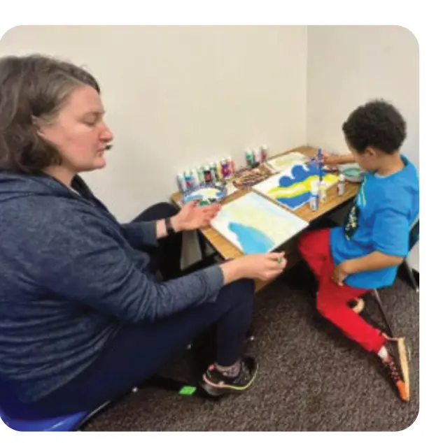 A mother and son sit side by side painting.