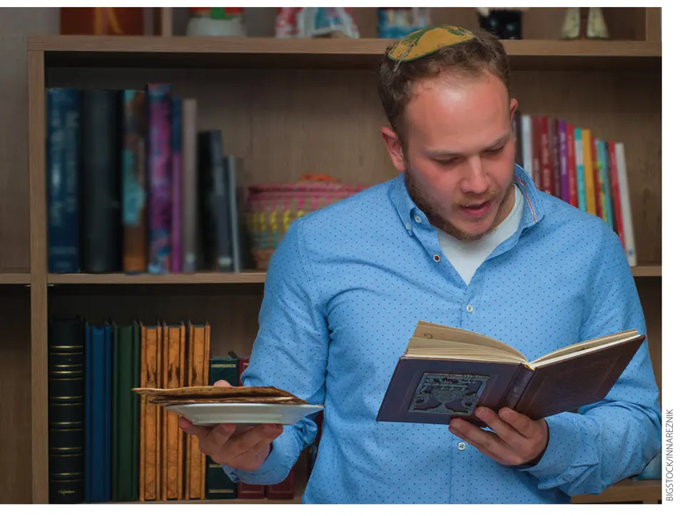 A man wearing a kippah reads from a Haggadah while holding a plate of matzah. (Bigstock/Innareznik)